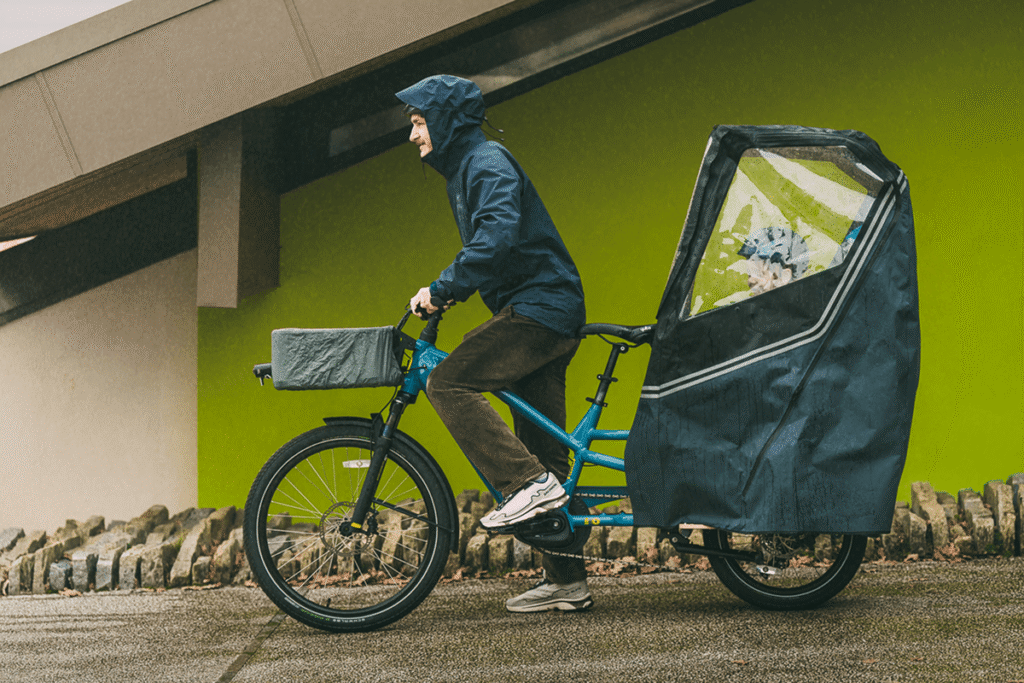 Parent wearing waterproof jacket on Yuba cargo bike with Pop Shelter rain cover